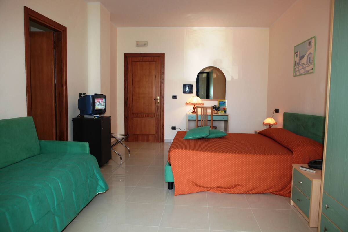 A bedroom with two beds, a desk, a chair, a television, and a lamp.
