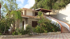 A stone house with a curved staircase leading to a wooden deck. - Hotel Village Eden (Ricadi)