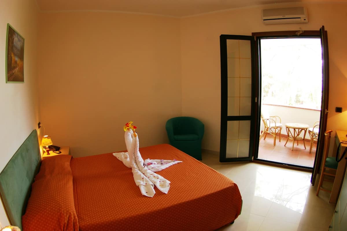 A hotel room with a bed, a chair, a table, and a balcony with chairs.