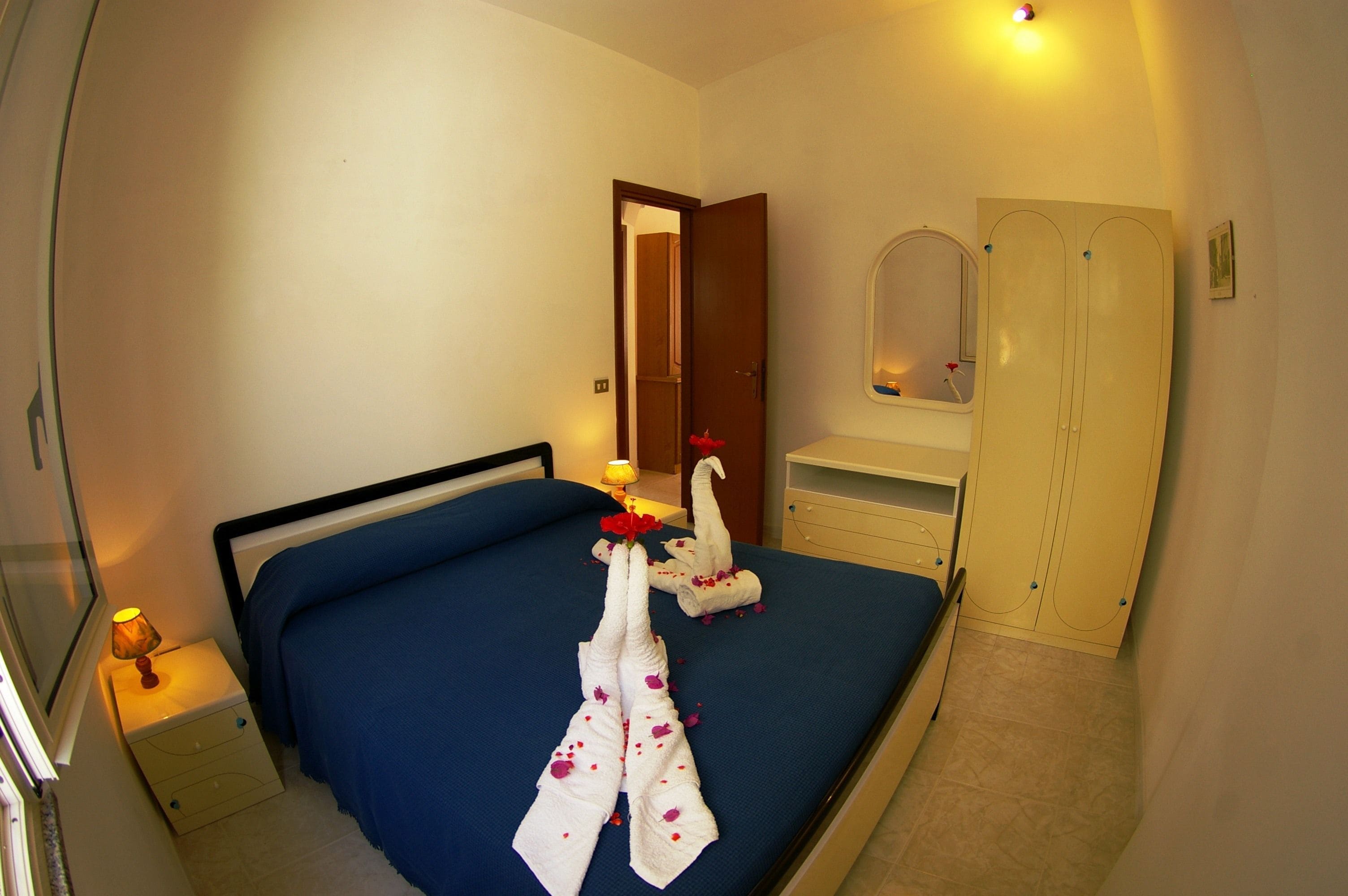 A hotel room with a bed, a nightstand, a wardrobe, and a mirror.