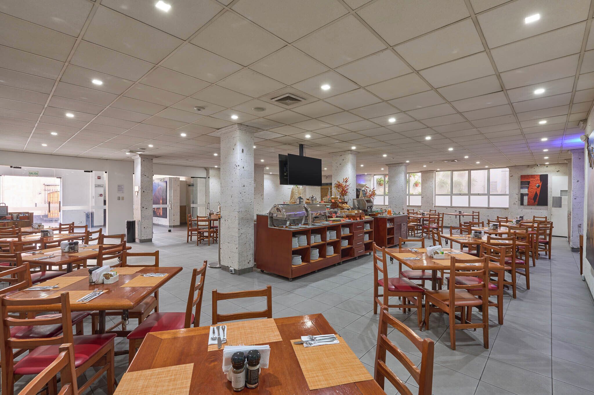 Un comedor amplio con varias mesas y sillas, una estación de buffet y un televisor montado en el techo.