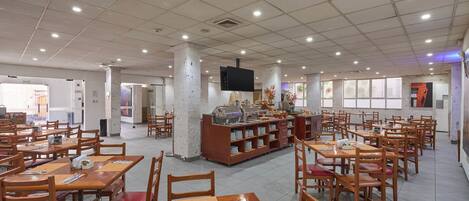 Un comedor amplio con varias mesas y sillas, una estación de buffet y un televisor montado en el techo.