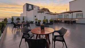 Un patio en la azotea con mesas y sillas de madera redondas, plantas en macetas y sombrillas.