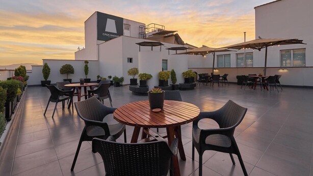 Un patio en la azotea con mesas y sillas de madera redondas, plantas en macetas y sombrillas.