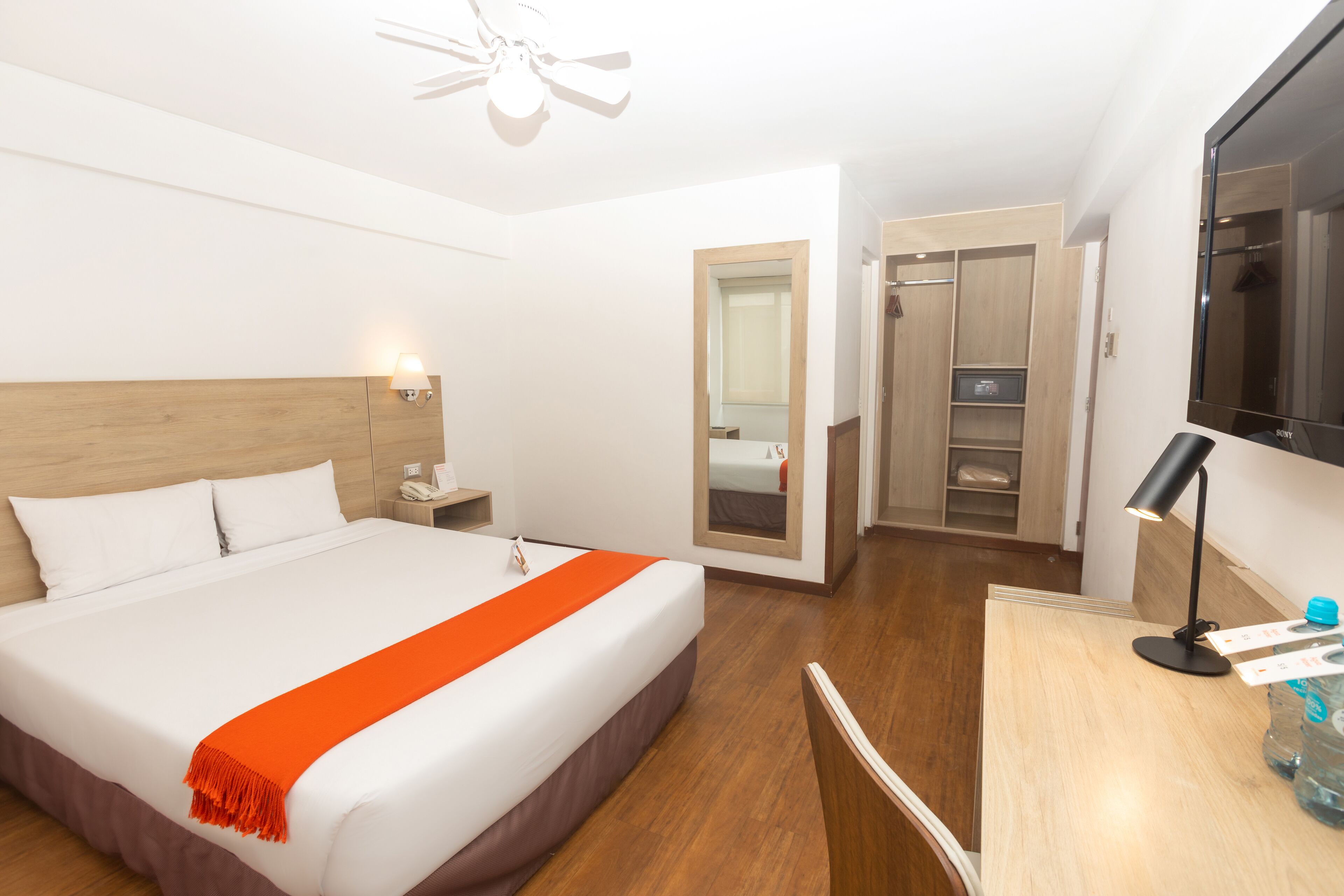 Une chambre d’hôtel avec un grand lit, un bureau avec une lampe, une armoire et un miroir.