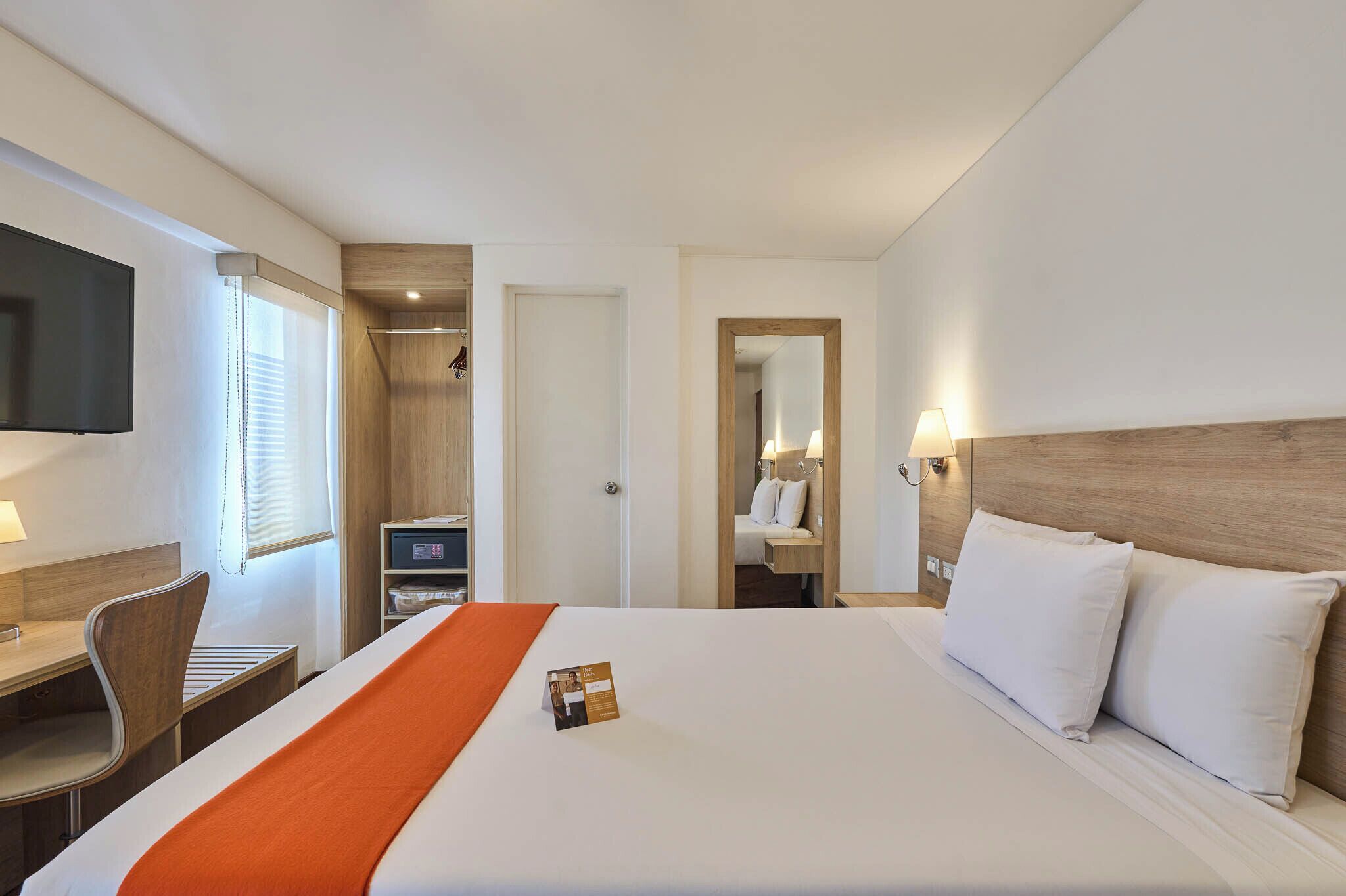 A hotel room with a bed, a desk, a TV, a mirror, and a wardrobe.