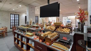 Zona de bufé con diferentes opciones de comida, un televisor de pantalla plana y una planta decorativa.