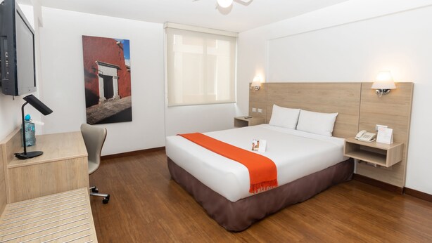 Una habitación de hotel con cama, escritorio, silla y televisión en la pared.
