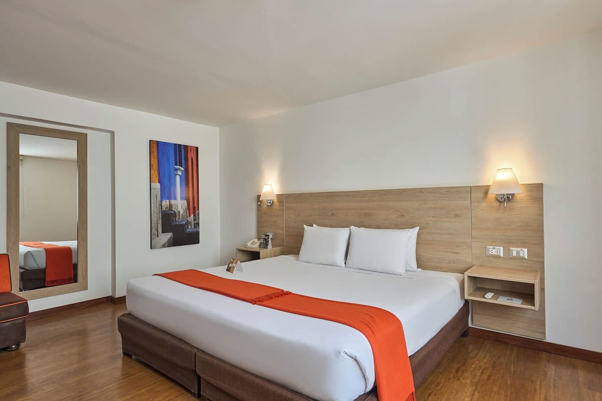 Ein Hotelzimmer mit einem großen Bett, einem Nachttisch, einer Wandleuchte und einem Gemälde.
