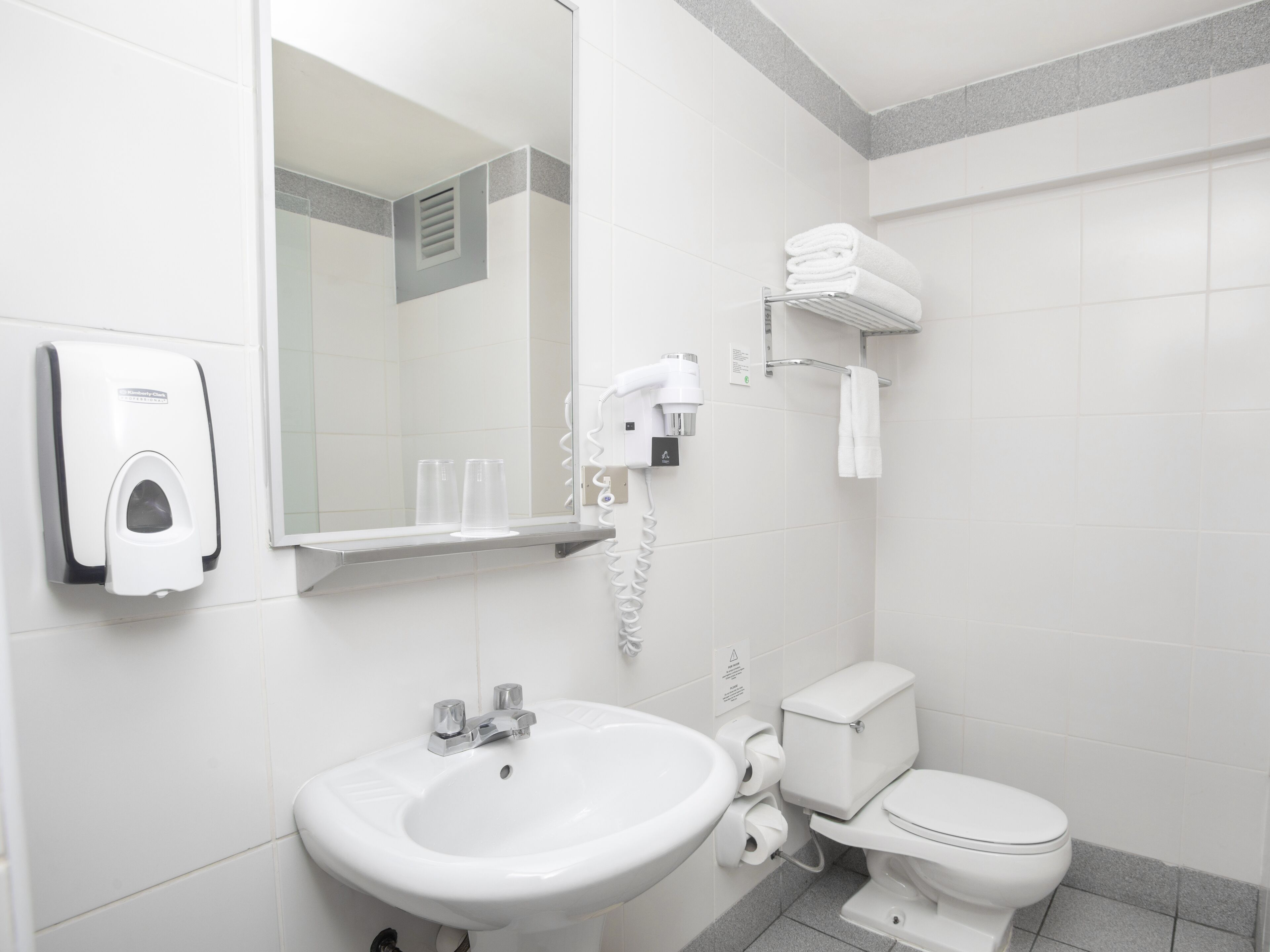 Une salle de bain moderne équipée d’un lavabo, de toilettes, d’un sèche-mains et d’un porte-serviettes.