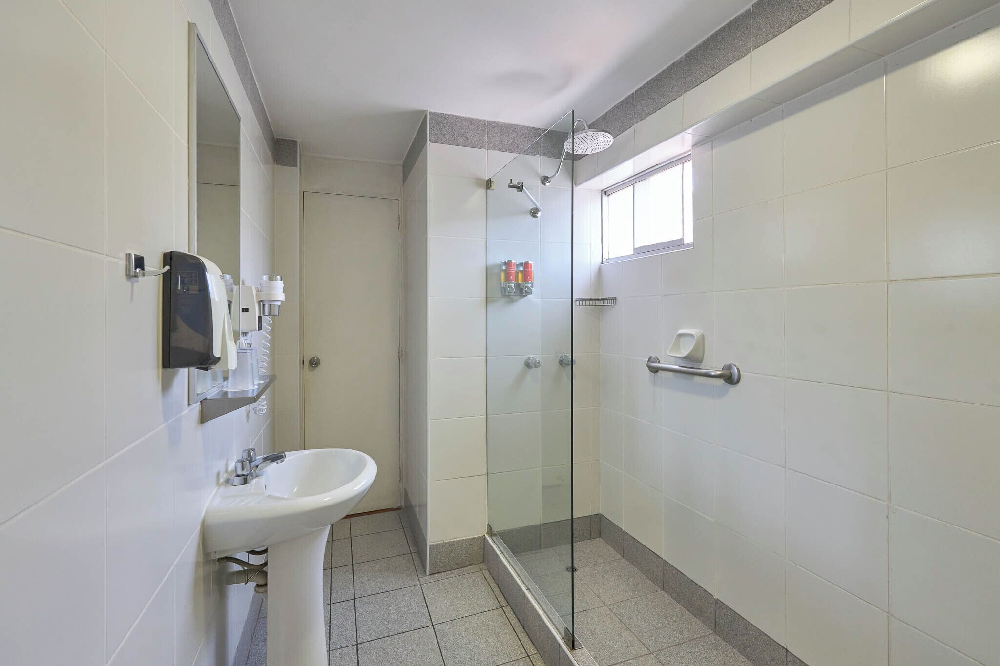 Een badkamer met een douchecabine van glas, een wastafel en een handdroger.
