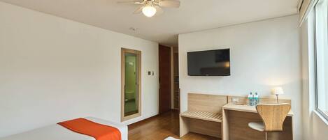 A hotel room with two beds, a desk, a chair, a television, and a ceiling fan.