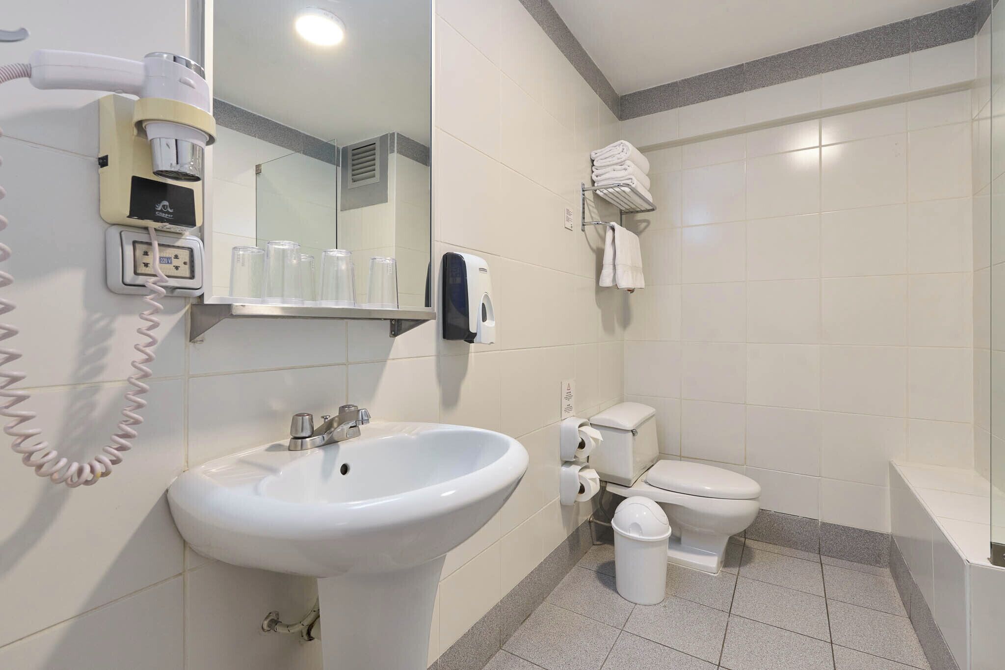 Un baño con lavamanos, inodoro, secador de manos y espejo.