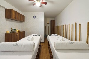 A spa room with two beds, a wooden cabinet, a clock, and a ceiling fan.