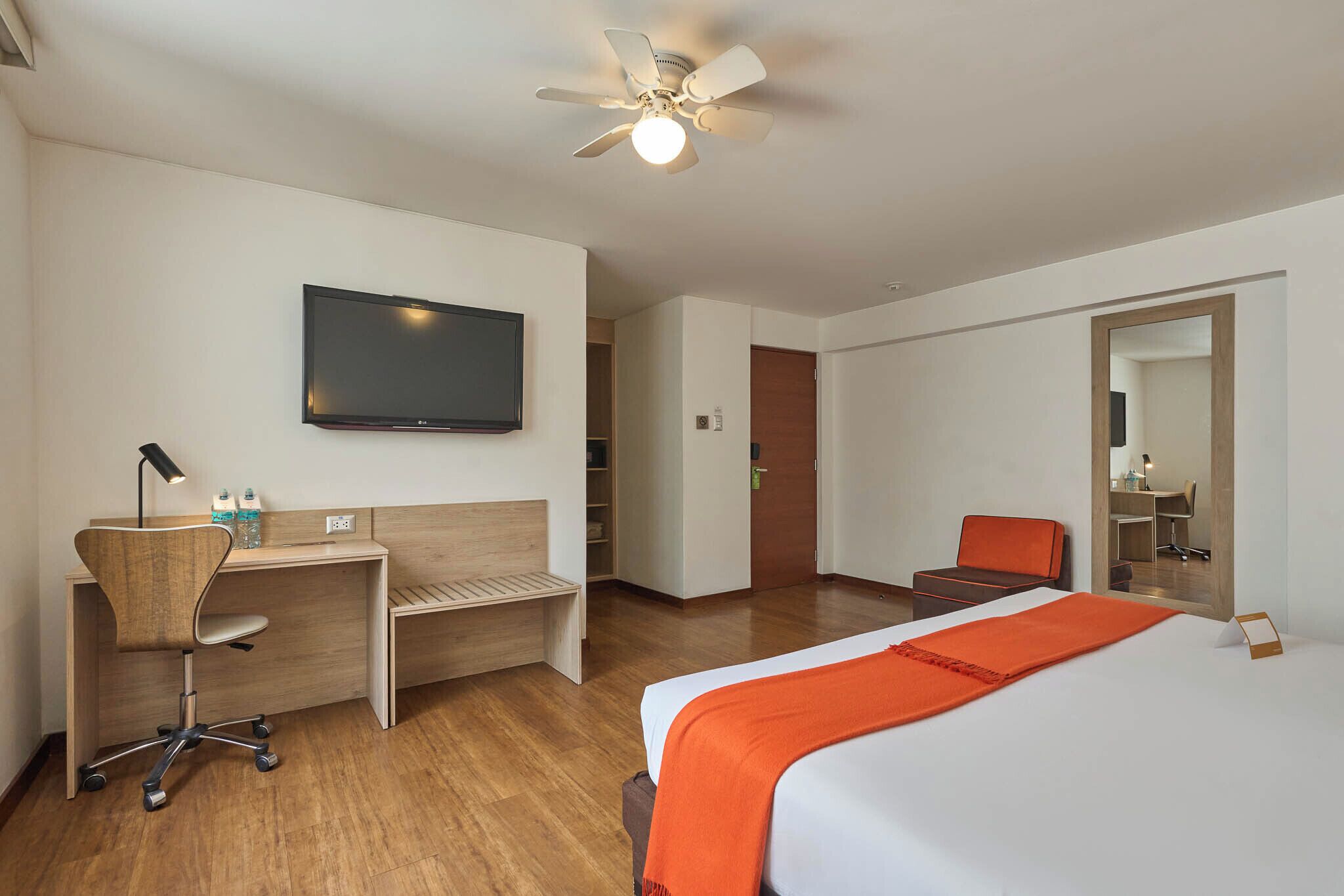 A hotel room with a bed, desk, chair, TV, and a ceiling fan.