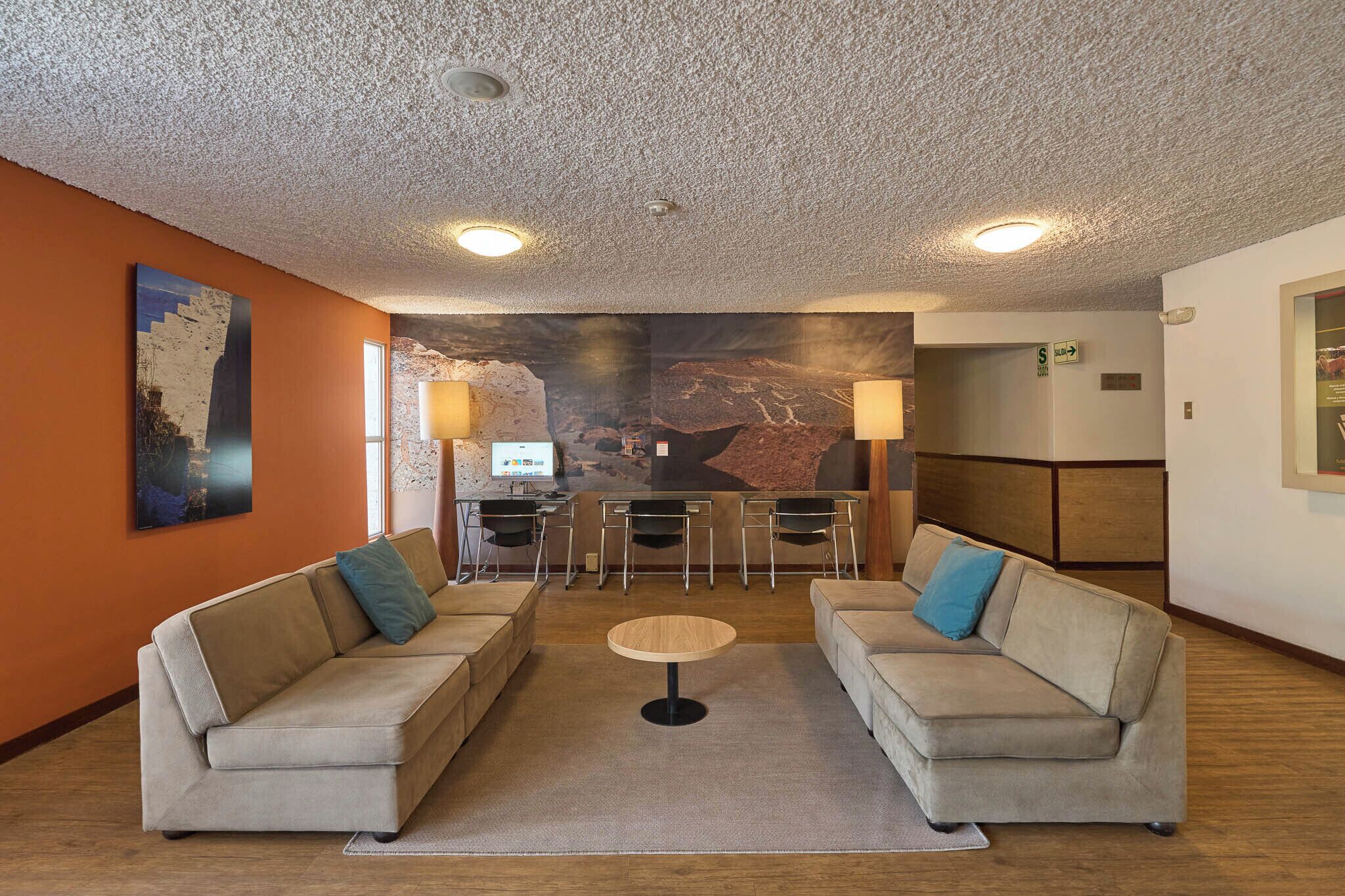 A lobby with two sofas, a small round table, a bar area, and a mural on the wall.