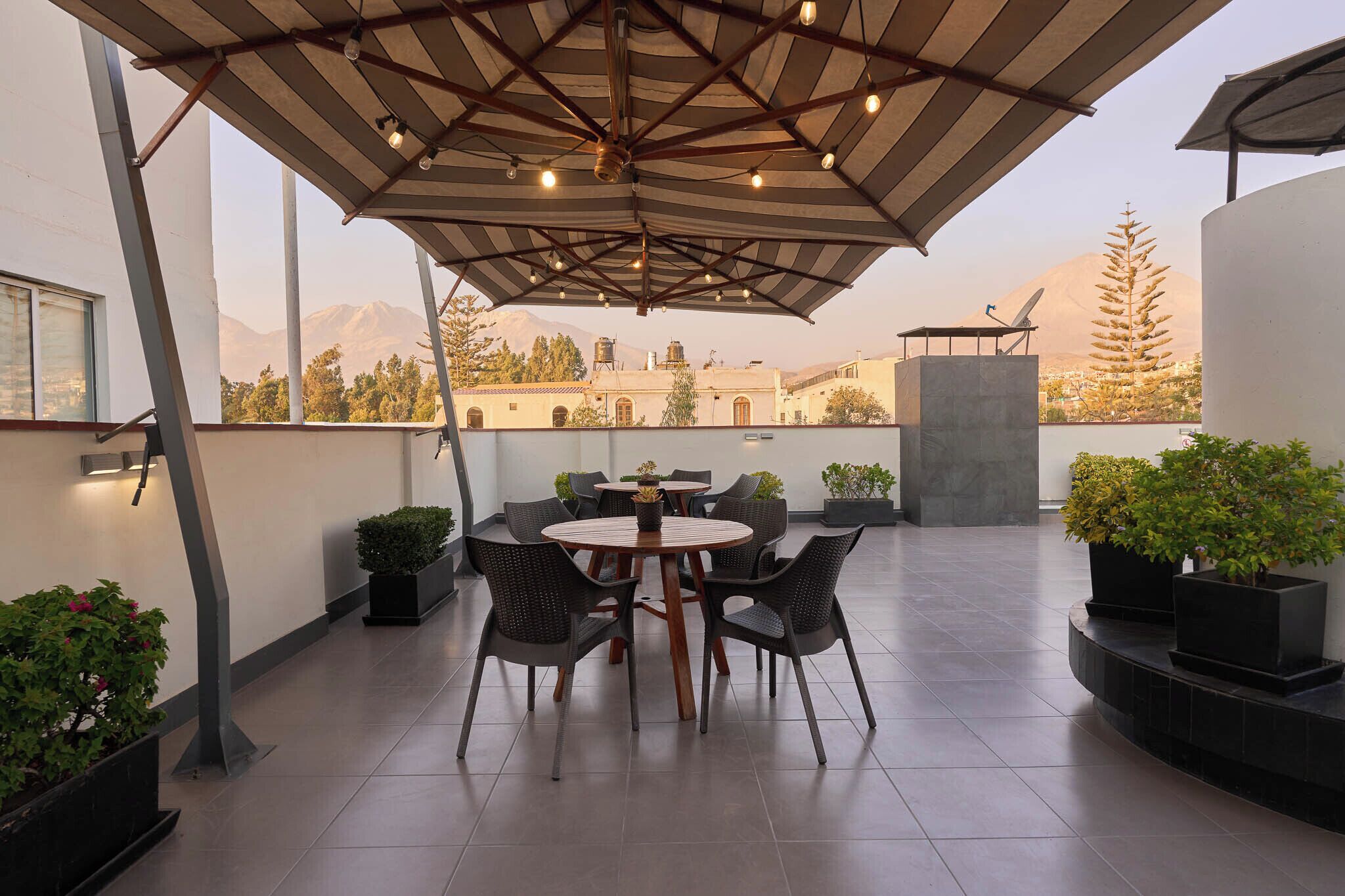 Una terraza con una mesa redonda y sillas, plantas en macetas y vistas a montañas.