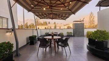 Una terraza con una mesa redonda y sillas, plantas en macetas y vistas a montañas.