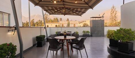 Una terraza con una mesa redonda y sillas, plantas en macetas y vistas a montañas.