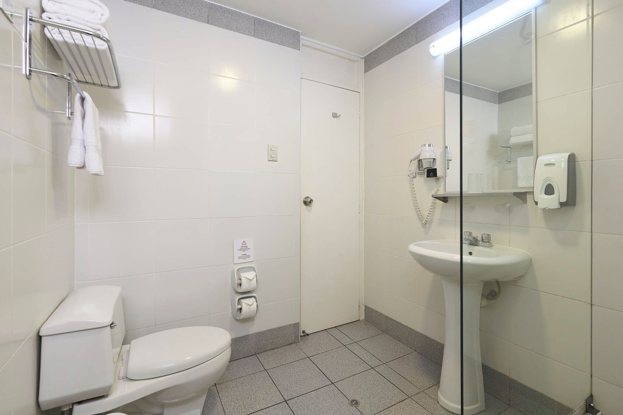 Un baño con inodoro, lavamanos, cabina de ducha de vidrio y toallero con toallas.