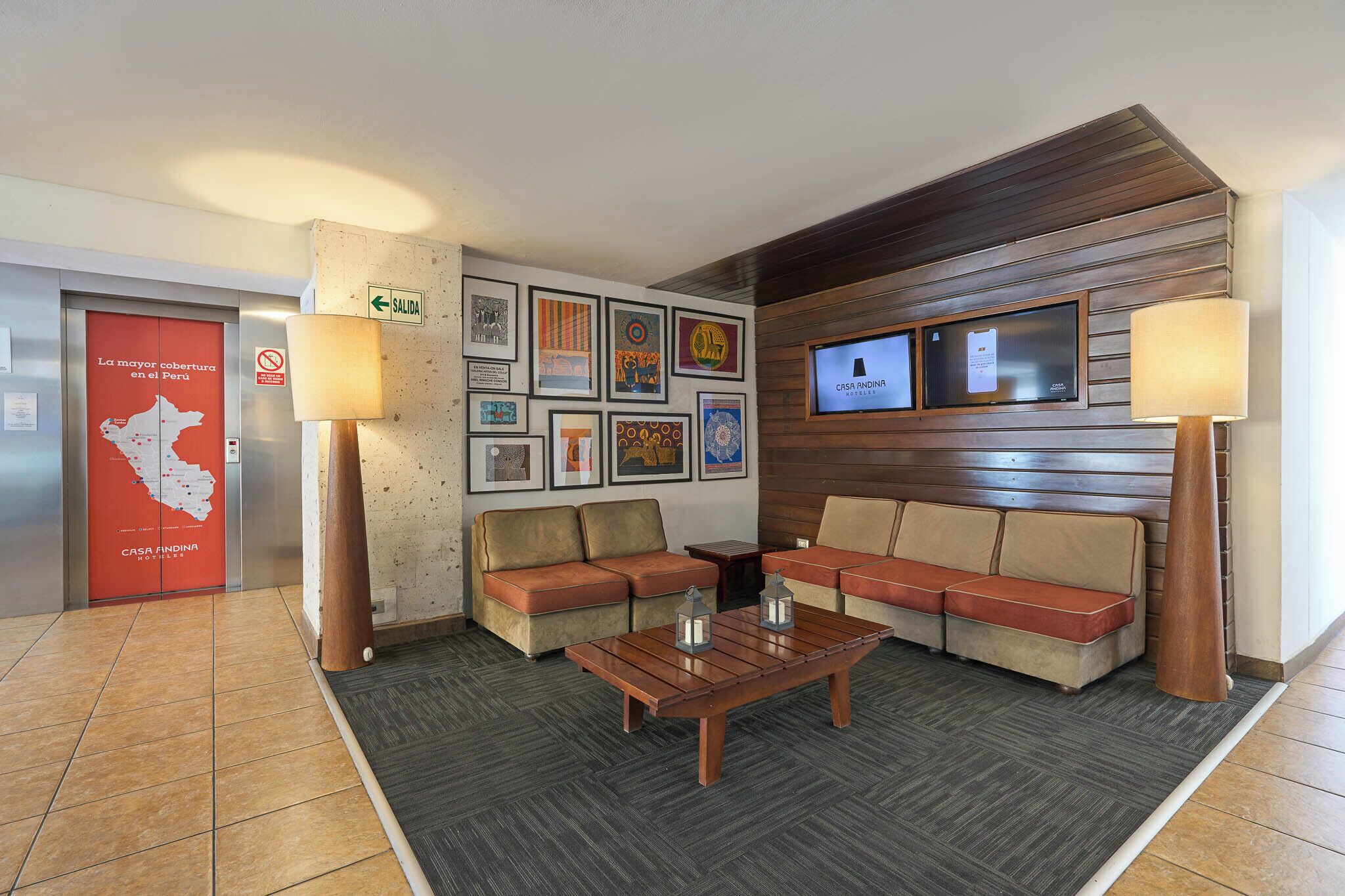 A lobby with a sofa set, a coffee table, wall-mounted TV, framed artwork, and a red exit sign.
