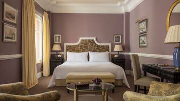 Habitación de hotel con una cama grande, dos mesitas de noche con lámparas, una mesa de centro redonda de vidrio y dos sillones tapizados.