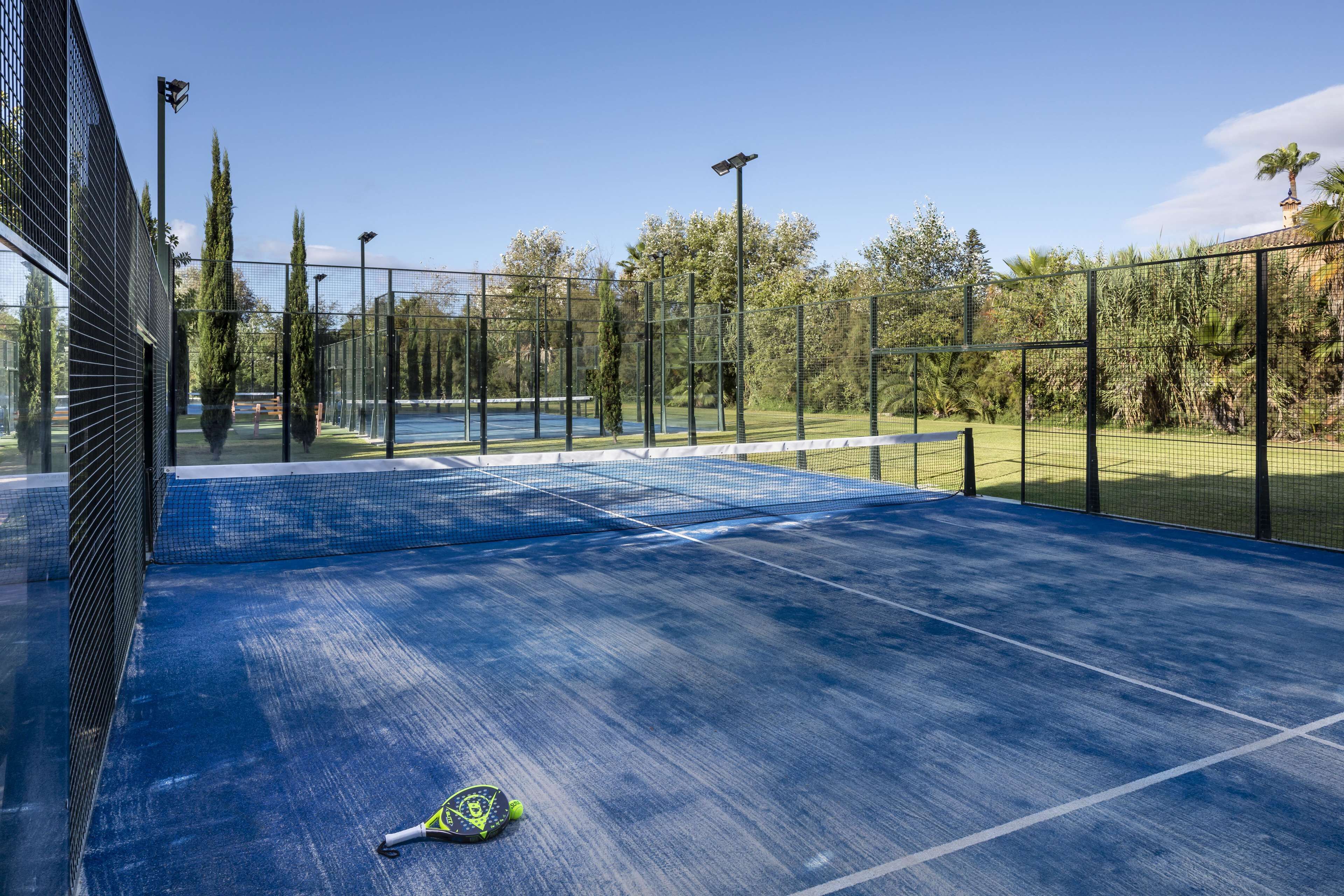 An outdoor tennis court with a net, surrounded by a fence, and trees in the background.