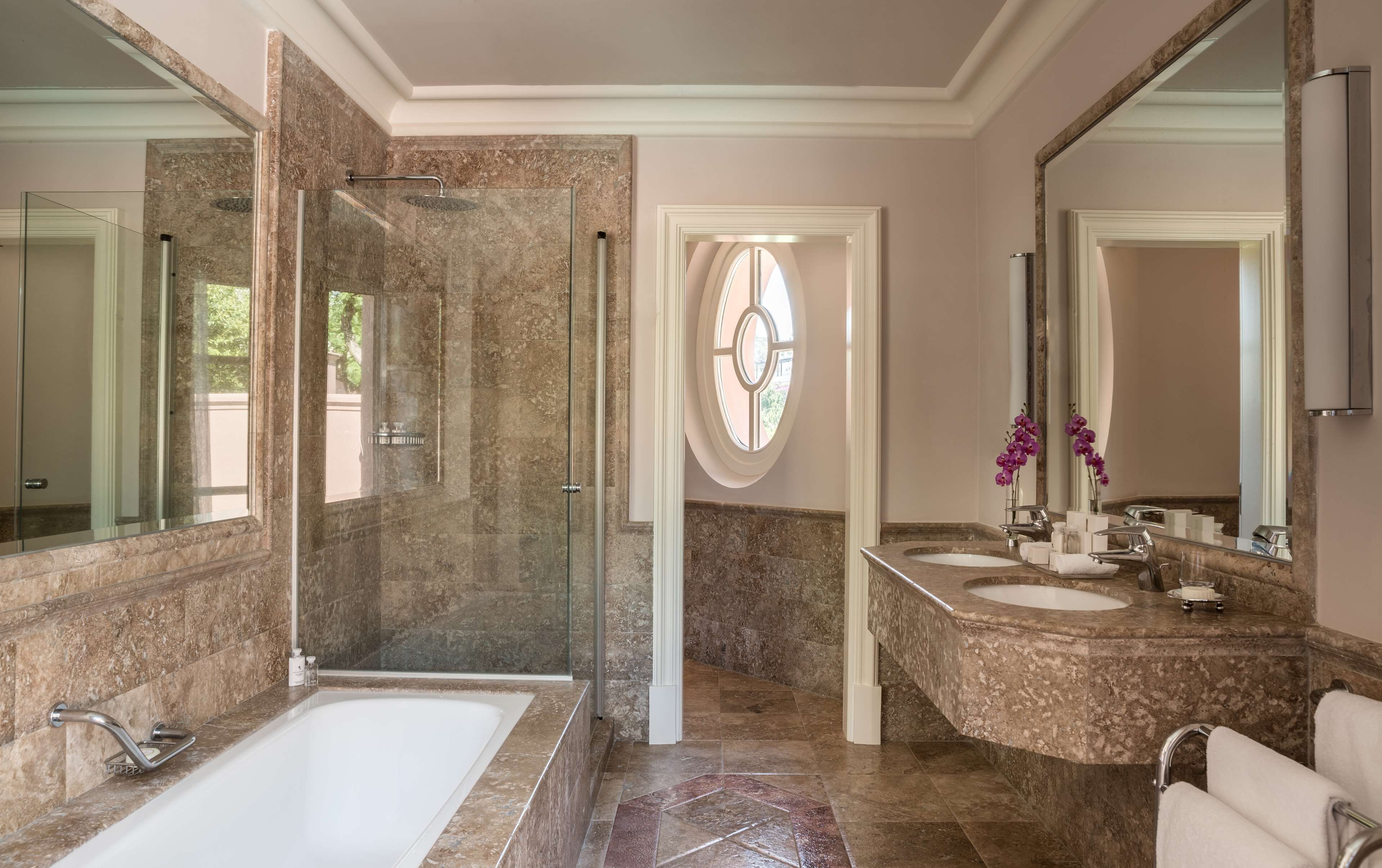 Un baño moderno con ducha de vidrio, una bañera independiente y un tocador con dos lavamanos.