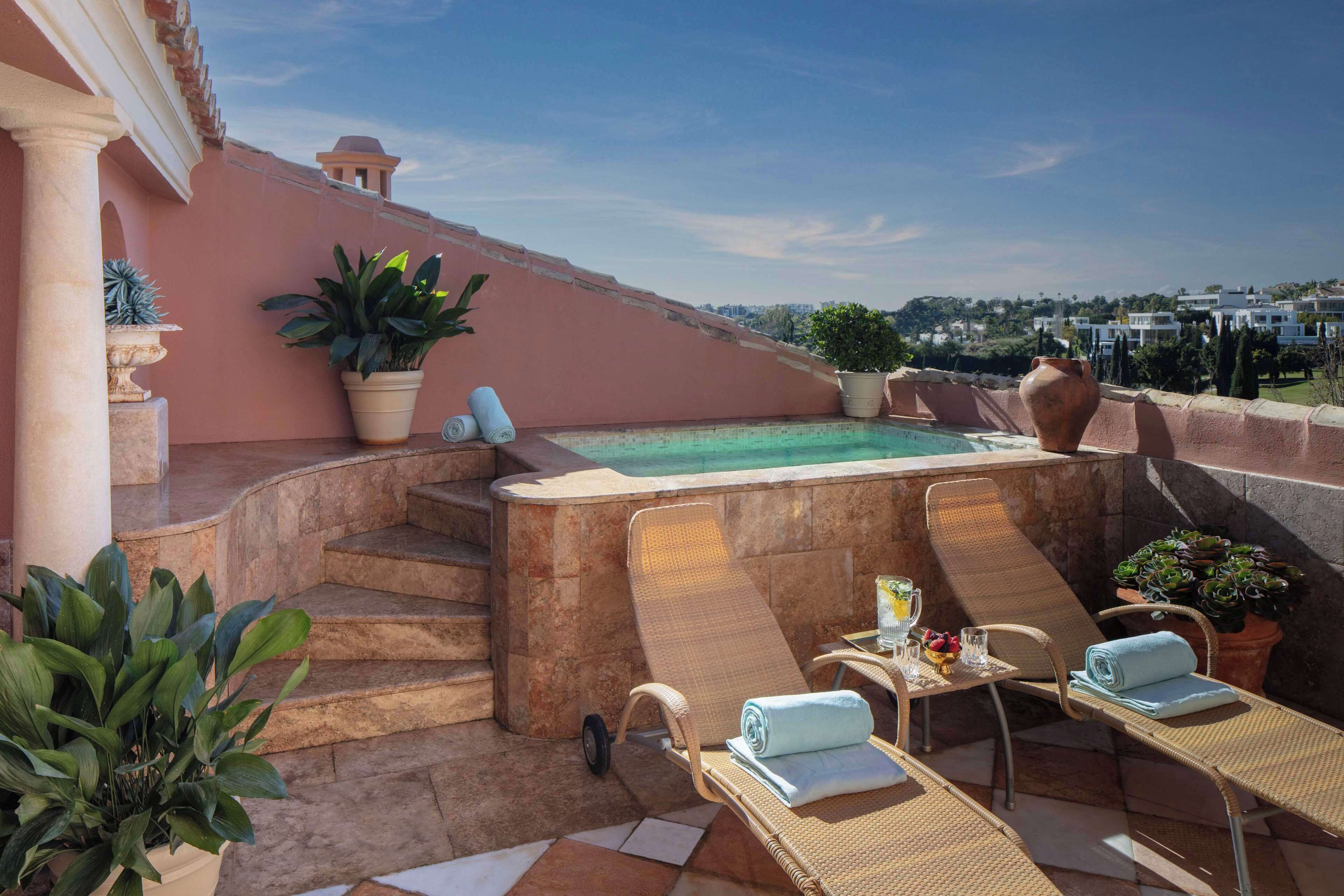 Een terras op het dak met een jacuzzi, lounge stoelen en potplanten.