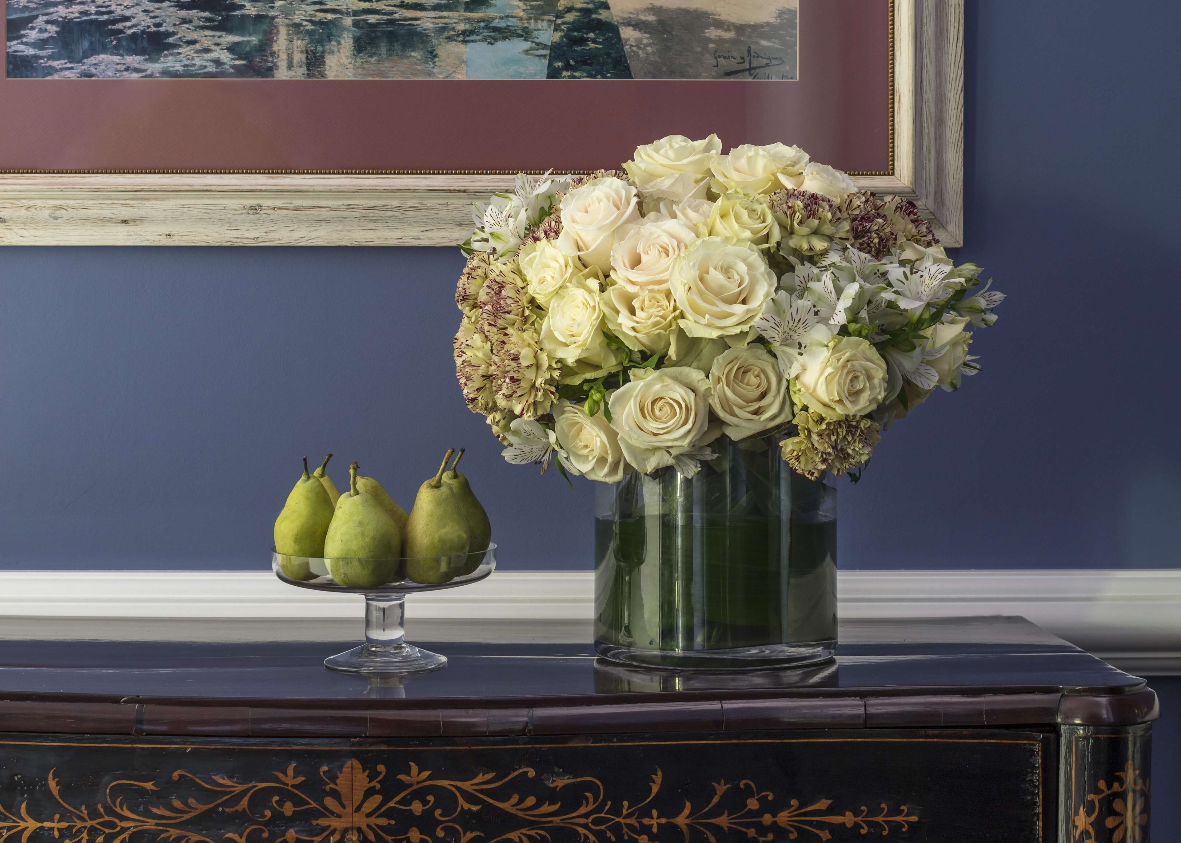 A vase of white flowers and pears on a dark wooden table against a blue wall.