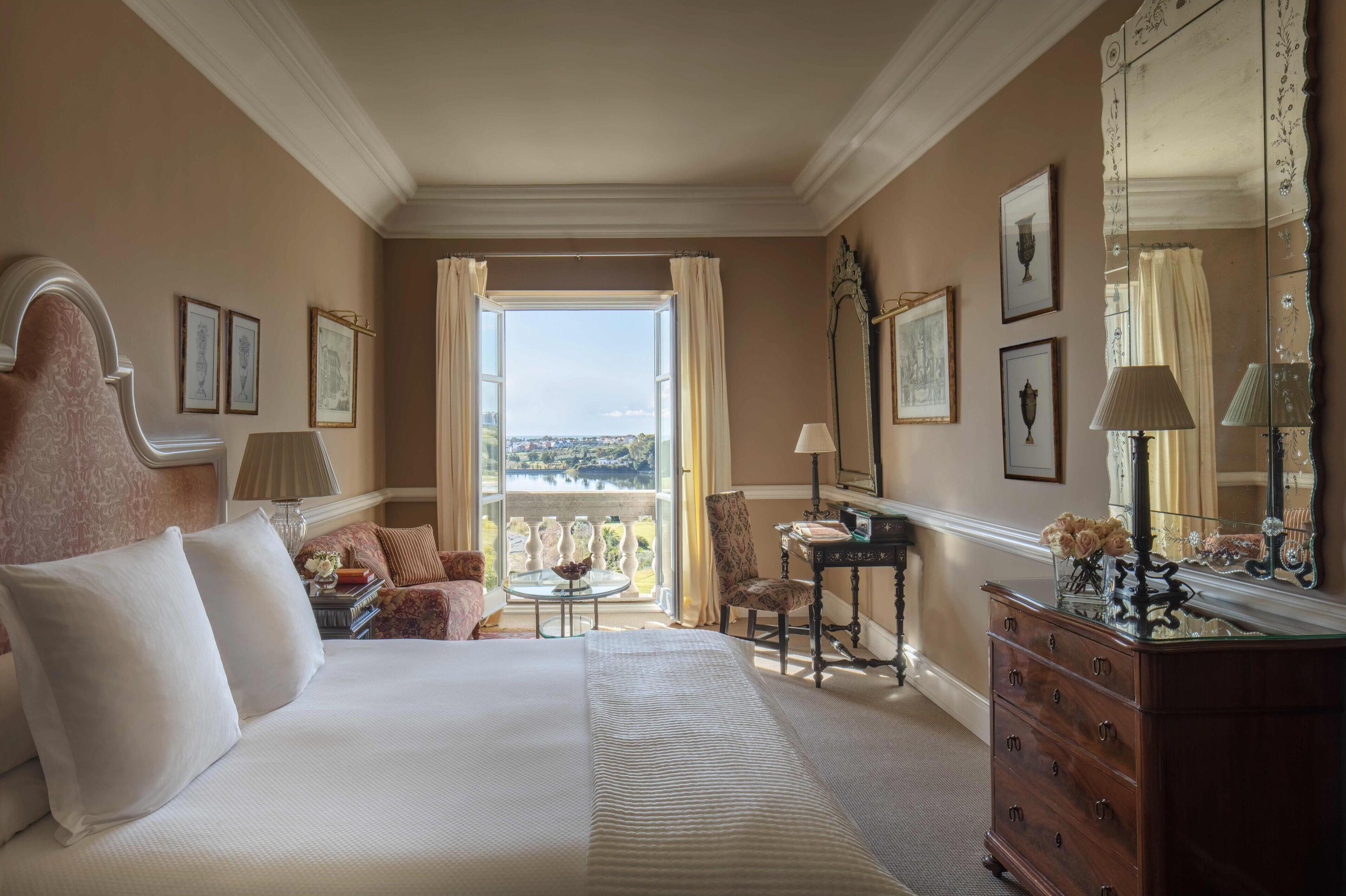 Une chambre d’hôtel avec un grand lit, un bureau, une chaise, une commode et un balcon avec vue.