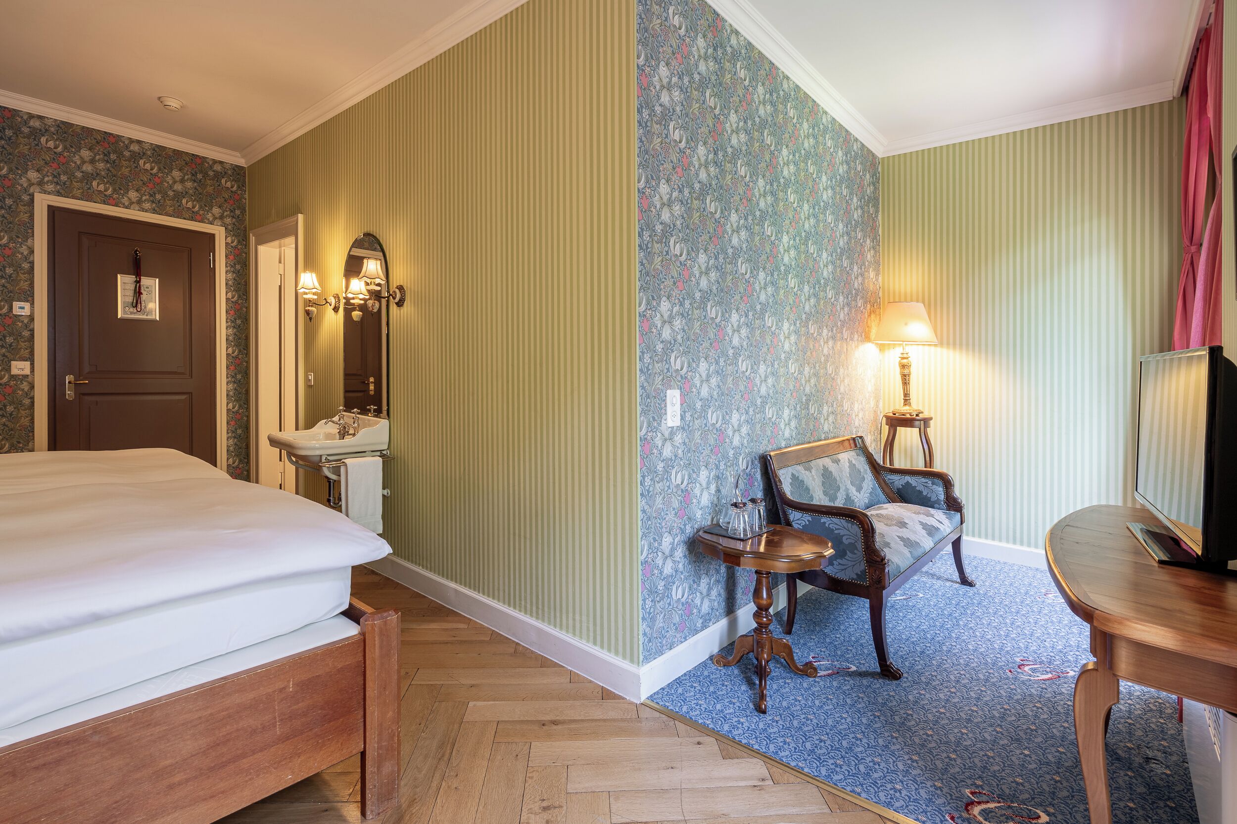 A hotel room with a bed, a vanity with a mirror, a chair, a table, and a television.
