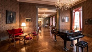 Une vaste pièce avec un magnifique piano à queue, un canapé rouge et un lustre.