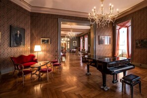 A grand room with a grand piano, a red sofa, and a chandelier. - Grandhotel Giessbach (Brienz)