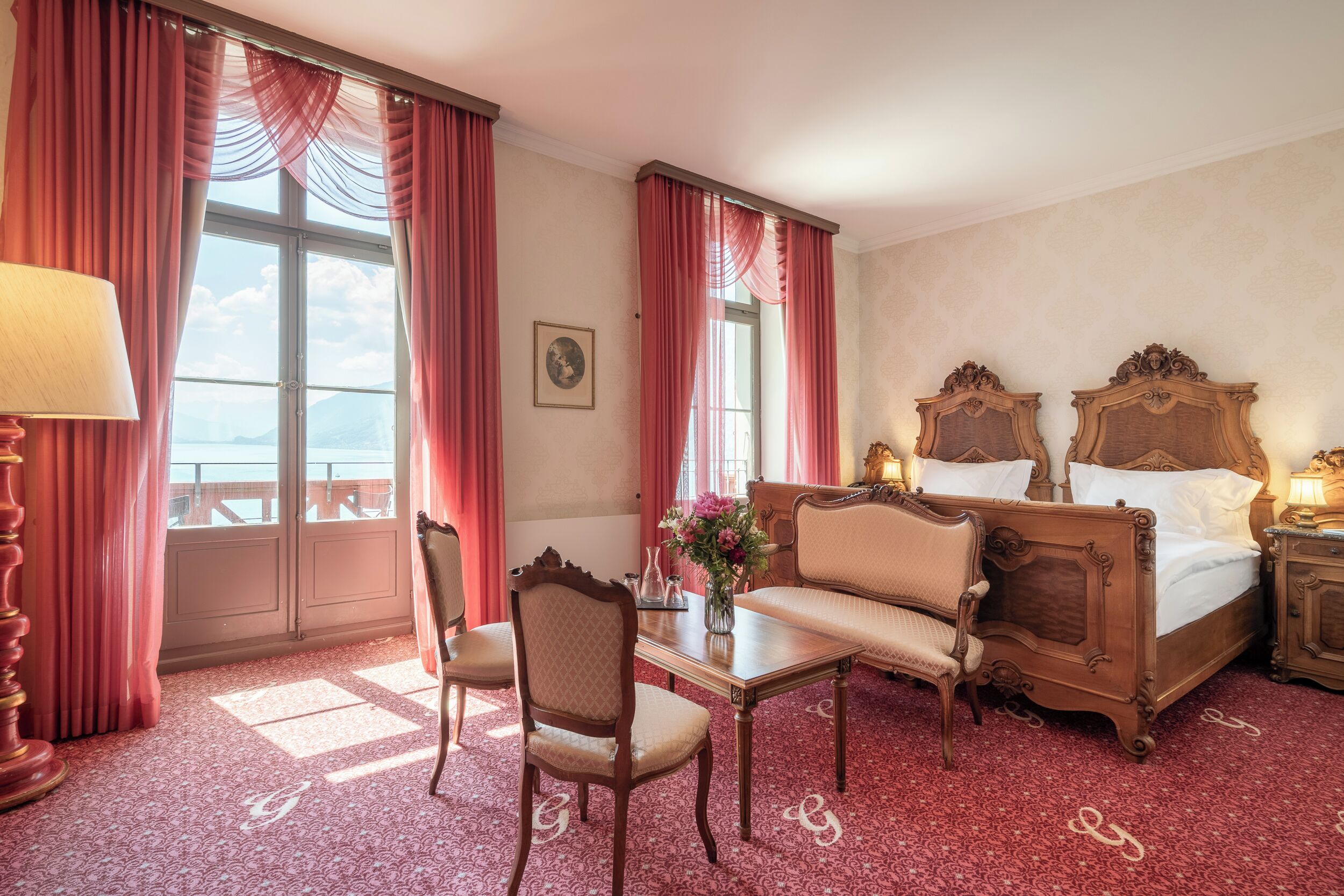 A hotel room with a large bed, a desk, a chair, and a view of the sea through the windows.