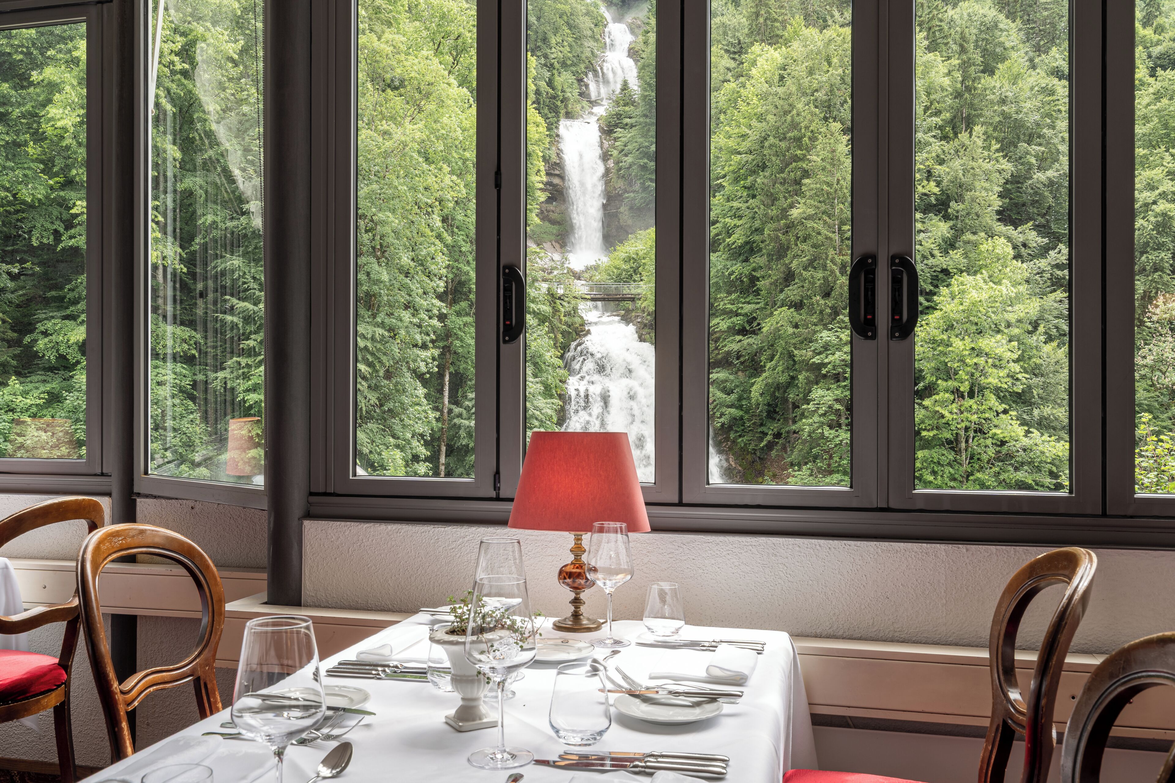 A dining table set for two with a view of a waterfall through large windows.