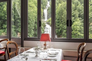 A dining table set for two with a view of a waterfall through large windows.