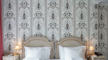 Habitación de hotel con cama clásica, dos mesitas de noche con lámparas y un papel tapiz decorativo con motivos florales.