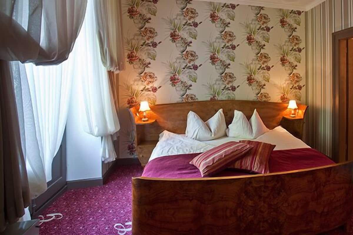 Quarto de hotel com cama de madeira, papel de parede floral e duas luminárias de cabeceira.