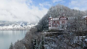 A snow-covered building with a tower, surrounded by a lake and forested mountains.