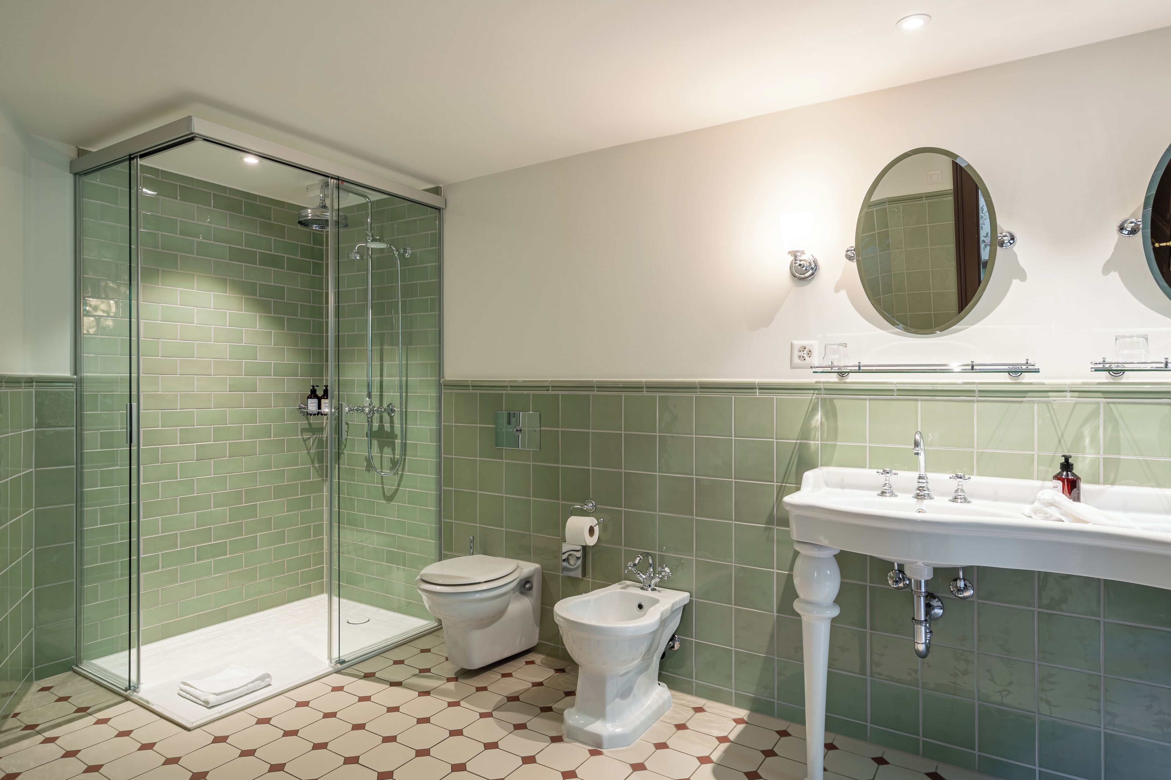 A bathroom with a glass-enclosed shower, a toilet, a bidet, and a sink with a mirror.