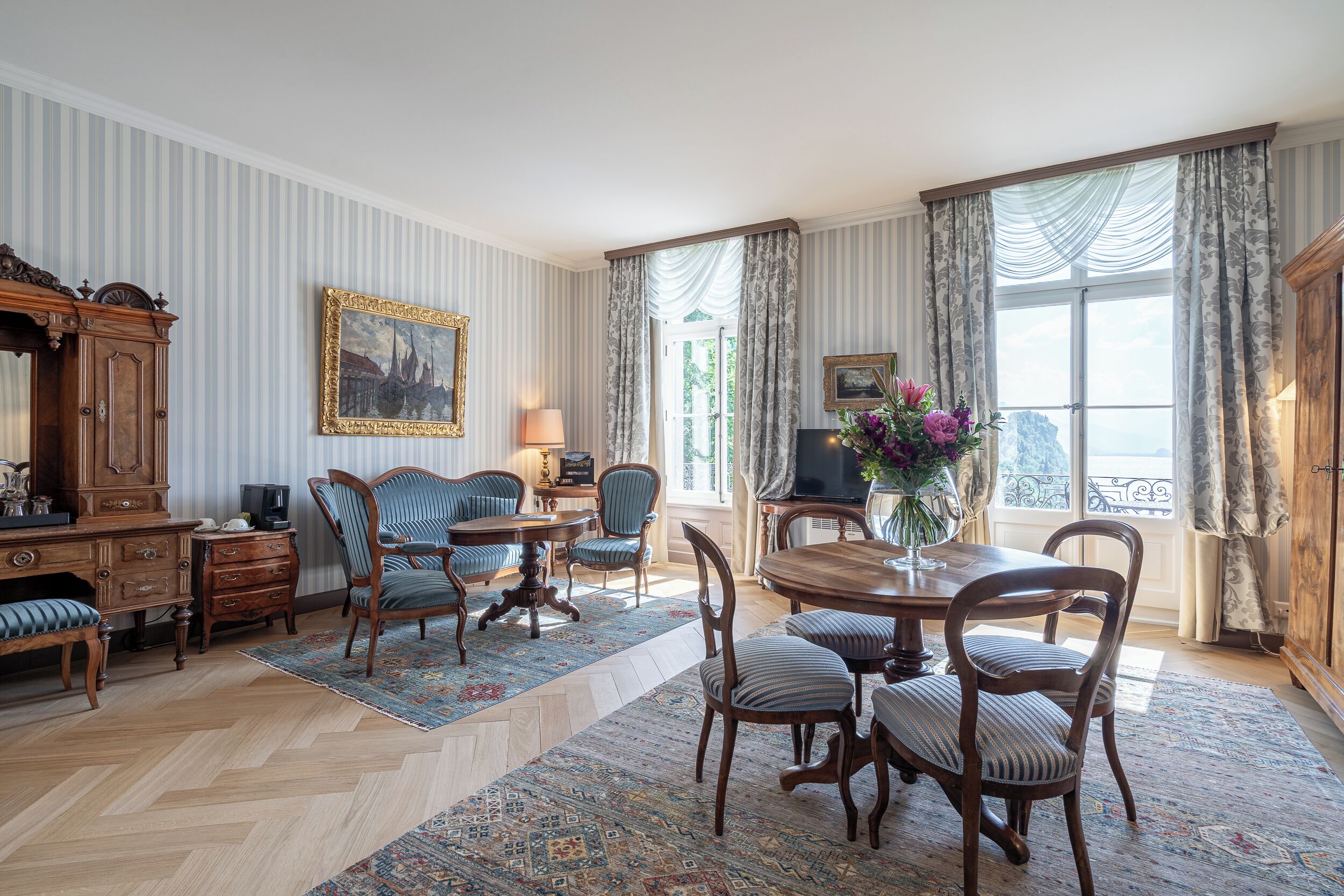 Ein traditionell eingerichtetes Zimmer mit Essbereich, Fernseher und einem großen Fenster mit Vorhängen.