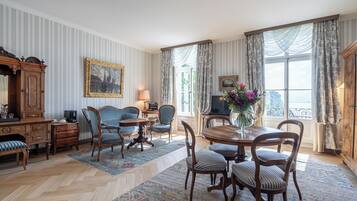 Ein traditionell eingerichtetes Zimmer mit Essbereich, Fernseher und einem großen Fenster mit Vorhängen.
