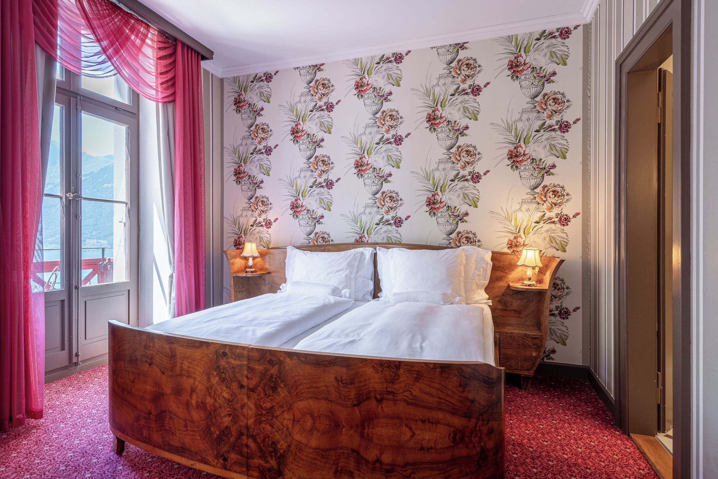 Ein Schlafzimmer mit einem hölzernen Bett, floralem Wandpapier und zwei Nachttischlampen.