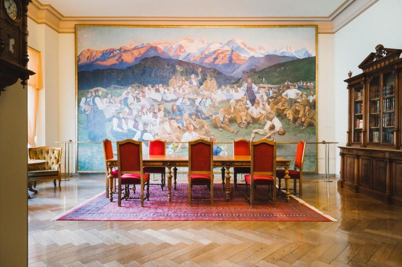 Un comedor con un gran mural de un paisaje montañoso, mesas y sillas de madera, y un suelo con patrón de espiga.