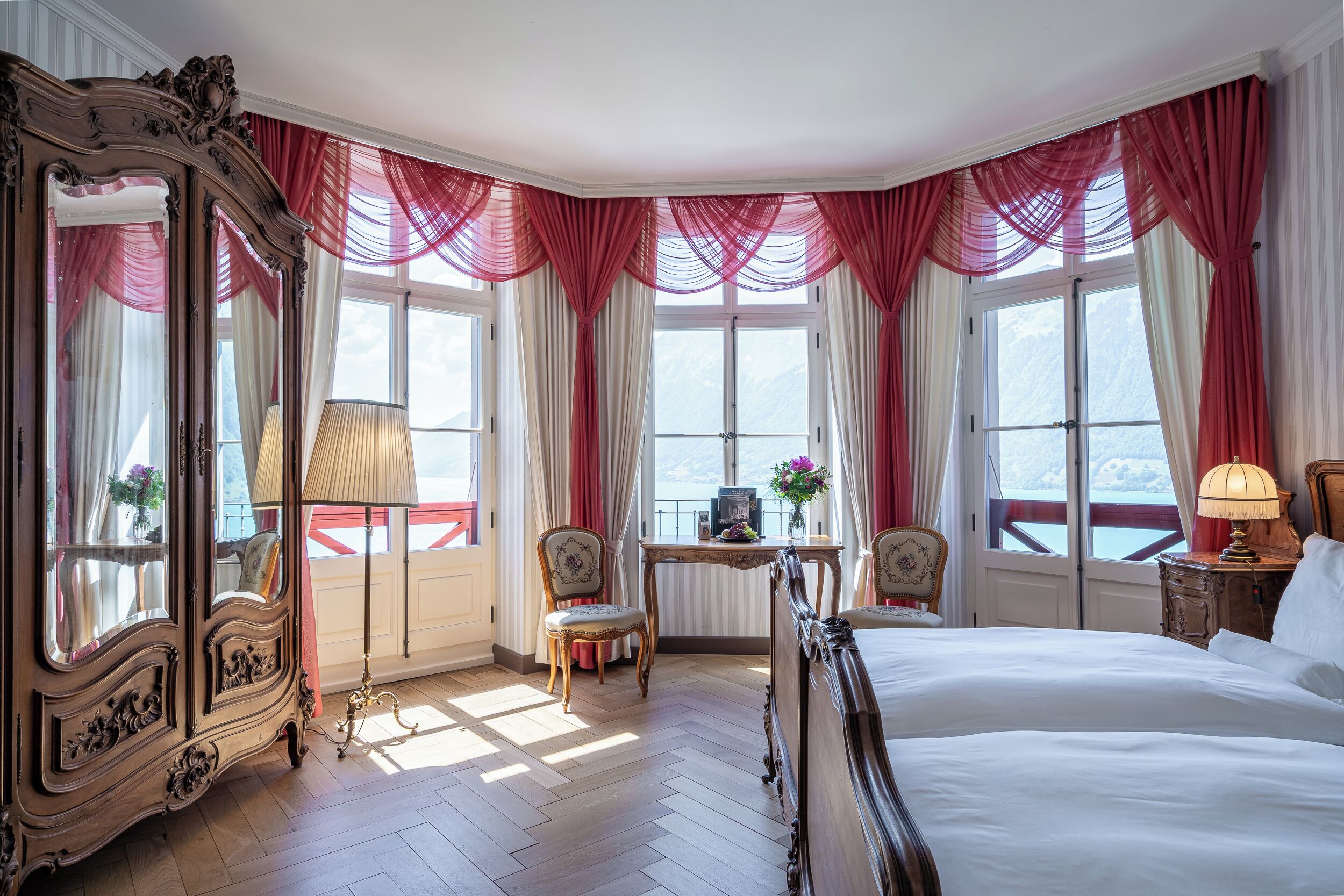 Une chambre d’hôtel avec un grand lit, deux fauteuils, un bureau et un grand miroir.