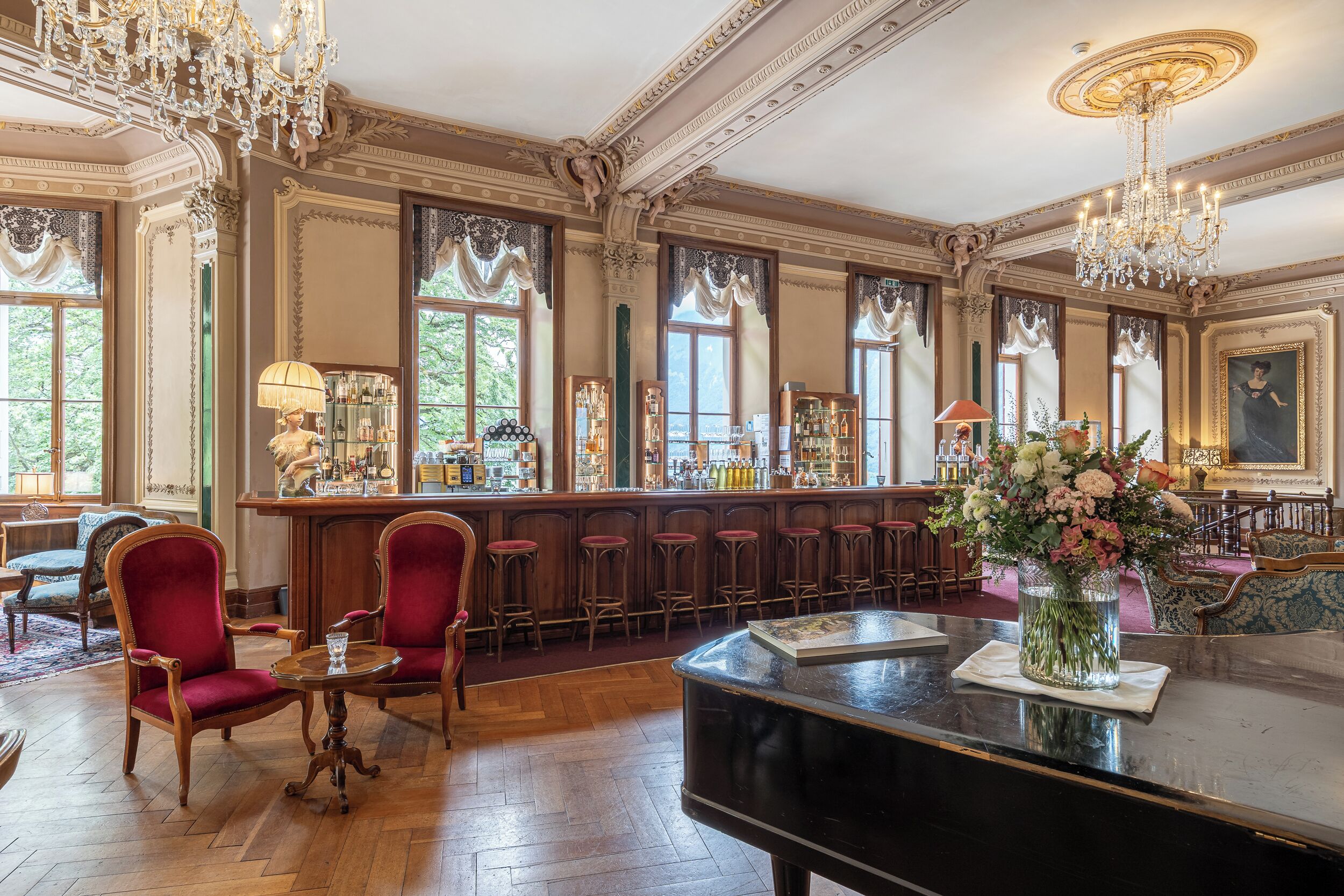A bar area with a piano, red upholstered chairs, and a bar counter with various bottles.