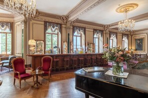Eine Bar mit Klavier, roten Sitzmöglichkeiten und einer Theke mit verschiedenen Flaschen.