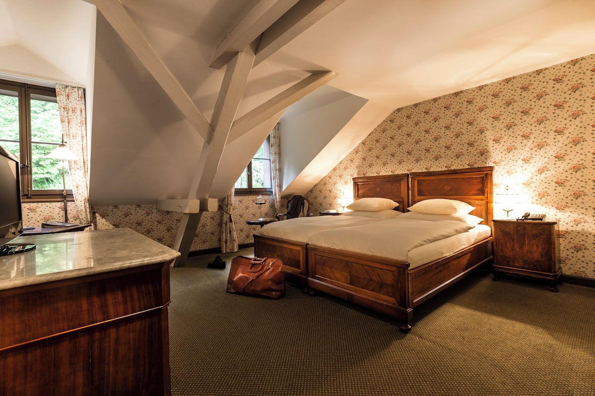 Quarto com cama de madeira, escrivaninha e janela com cortinas.