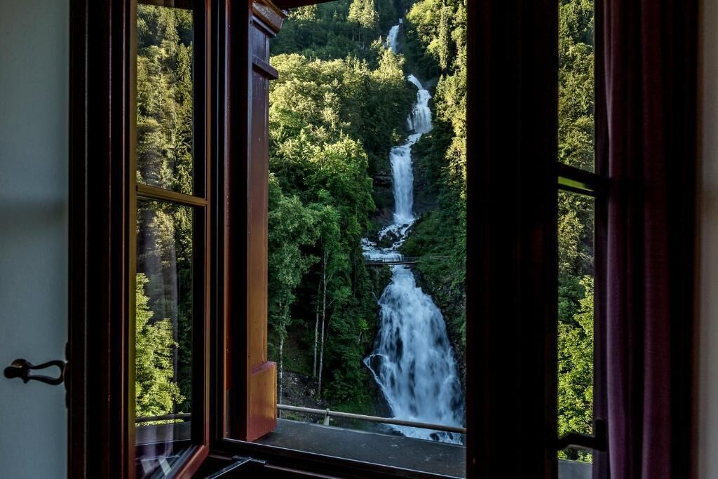 Vista de una cascada a través de un ventanal, rodeado de abundante vegetación.
